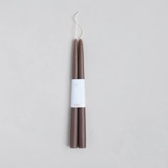 two brown candles sitting next to each other on a white surface with one candle in the middle