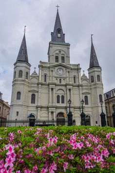 a large building with two towers and a clock on the front is surrounded by pink flowers