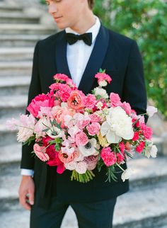 a man in a tuxedo holding a large bouquet of pink and white flowers