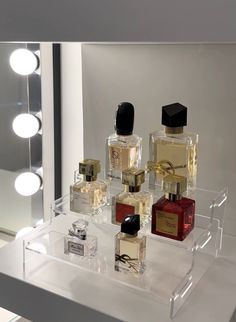 several different types of perfumes on display in front of a mirror with lights behind them