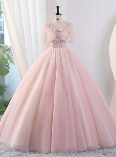 a pink ball gown with sequins on the top and sleeves is displayed in front of a window