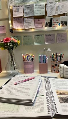 a desk with several notebooks, pens and flowers in a vase on top of it