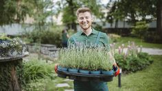 a man holding a tray full of plants in his hands and smiling at the camera