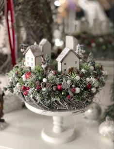 a christmas display with small houses and ornaments on top of a cake plate, surrounded by other holiday decorations