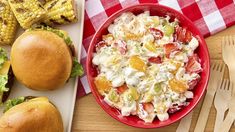 a table topped with sandwiches and salad next to corn on the cob, coleslaw