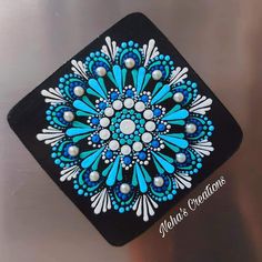 a blue and white design on a black square coaster with pearls in the center, sitting on a metallic surface