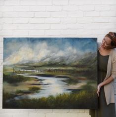 a woman standing next to a painting holding it up in front of her face and smiling