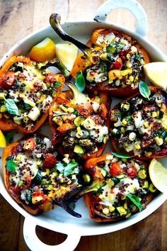 a white dish filled with stuffed peppers covered in cheese and herbs next to lemon wedges