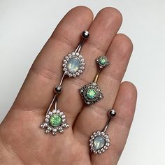 a person is holding three different types of piercings in their hand, one with green and white stones on it