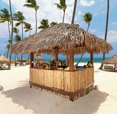 a tiki bar on the beach with palm trees and blue water in the background