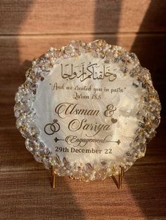 a glass plaque with the names of two people in arabic and english on it, sitting on a wooden surface