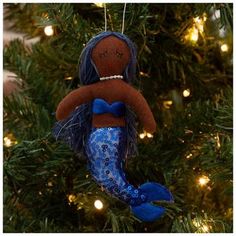 a christmas ornament with a mermaid doll hanging from it's side on a tree