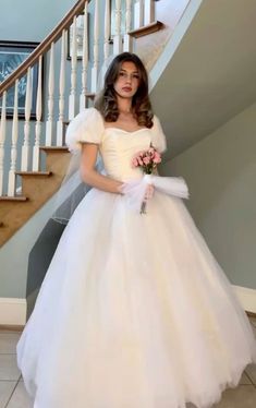 a woman in a white dress standing next to a stair case and holding a bouquet