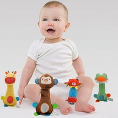 a baby sitting on the ground with toys around him and smiling at the camera while wearing a white bodysuit