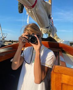 a woman holding a camera up to her face while standing on the deck of a boat