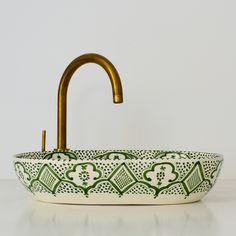 a green and white bowl with a golden faucet on it's side