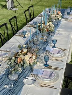 the table is set with blue and white plates, silverware, flowers and candles