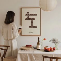 a woman standing next to a table holding a glass of wine in front of a crossword poster