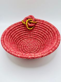 a red woven basket with a yellow bead decoration on the top and bottom, sitting on a white surface