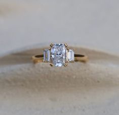 an engagement ring with three stones in it on top of sand covered flooring area