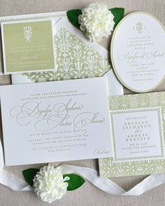 the wedding stationery is laid out on top of each other, with white flowers and green leaves