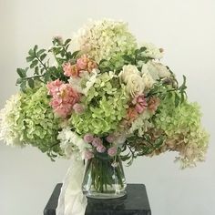 a vase filled with white and pink flowers on top of a black table next to a wall