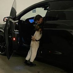 a man standing next to a black car with its door open and his hand on the door handle