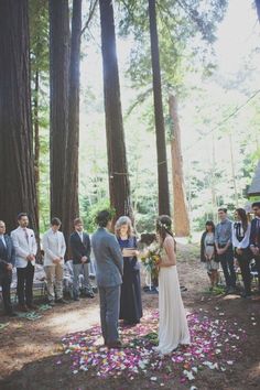 a couple getting married in the woods with flowers on the ground and people standing around