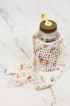 a water bottle with a crochet pattern on it sitting on a marble surface