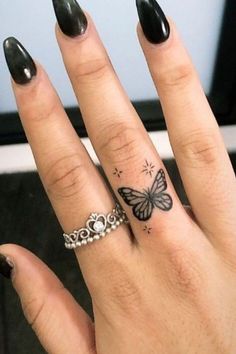 a woman's hand with a butterfly tattoo on her left ring and black nail polish