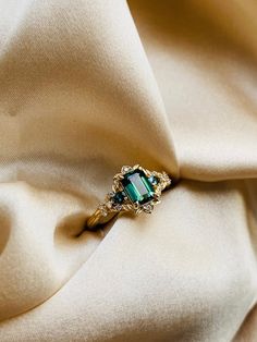 an emerald colored ring sitting on top of a white cloth with gold trimmings