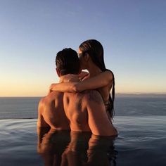 two people sitting on the back of a swimming pool with their arms around each other