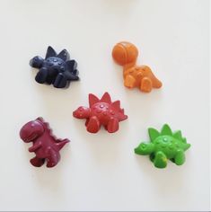 five different colored plastic dinosaurs on a white surface