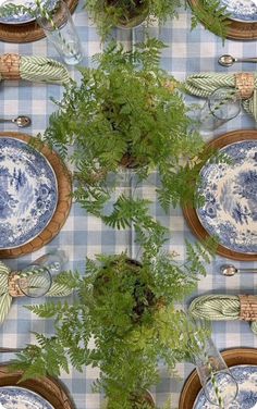 the table is set with blue and white plates, silverware, ferns and glass vases