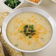 a white bowl filled with soup next to bowls of green onions and cheese on a table