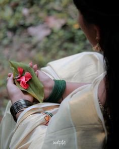 a woman in a white sari holding a red flower on her left hand and wearing green bracelets