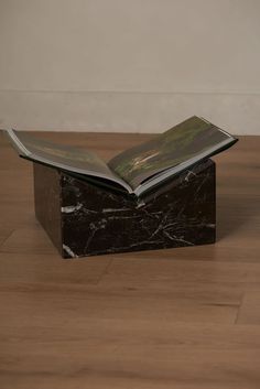 an open book sitting on top of a black marble block in the middle of a wooden floor