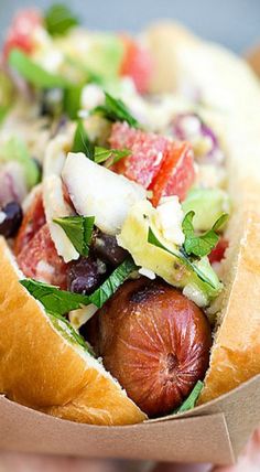 a close up of a person holding a hot dog in a bun with toppings