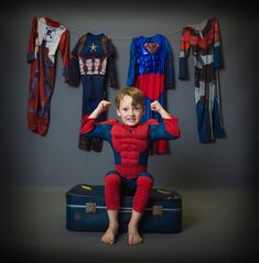 a young boy sitting on top of a suitcase in front of clothes hanging from a line