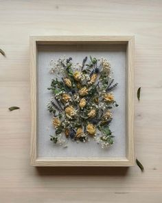 a frame with dried flowers in it on a wooden table next to leaves and twigs