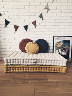 a bed with pillows on it in front of a white brick wall and some pictures