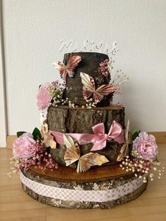 a three tiered cake with pink flowers and butterflies on the top is sitting on a wooden stand