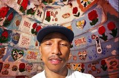 a man wearing a hat standing in front of a wall covered with patches and flowers