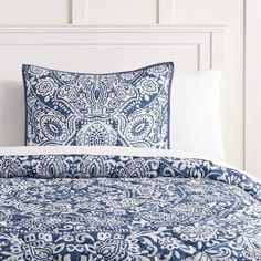 the blue and white bedding is neatly made with an intricate pattern on it's pillow