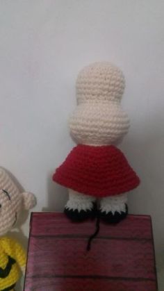 two crocheted dolls sitting next to each other on a wooden table with a white wall behind them