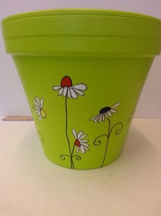 a green flower pot with daisies painted on it