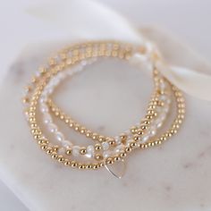 This stunning stack of dainty bracelets, feature a luxurious mix of gold-filled beads, freshwater pearls, and sparkly crystal zircon. This bracelet stack is a great set for instant impact or wear them separately to create multiple looks. This stack of five stretch bracelets includes: 1 - 4mm 14K gold filled bead bracelet 1 - 3mm 14K gold filled bead bracelet with silver floating heart 1 - 2.5mm 14K gold filled bead bracelet 1 - 3mm freshwater pearl stretch bracelet 1 - 3mm grade Aa  geuine cryst Gold Pearl Bracelet With Tiny Beads For Weddings, Gold Delicate Stackable Beaded Bracelets, Elegant Gold Charm Bracelet With Faceted Beads, Delicate Gold Stackable Beaded Bracelets, Dainty Pearl Stackable Beaded Bracelets, Dainty Stackable Pearl Beaded Bracelets, Stackable Pearl Beaded Bracelets As Gift, Elegant Gold Crystal Bracelet With Tiny Beads, Gold Beaded Bracelets With Tiny Beads For Wedding