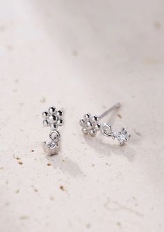 Made from solid 925 sterling silver, these are small stud earrings that have a delicate metallic flower with six 'petals' that sits on the ear lobe, a tiny square zirconia hanging underneath and silver butterfly clasps. Compact, with a timeless design, these studs will pair well with other delicate hoops or studs. 🎁 Packaging: Beautifully packed in a box, ready for gifting. 🏷️ This product is made of sterling silver -- easily recognizable by its '925' stamp of authenticity. It is also hypoallergenic, making it suitable for people with sensitive or irritable skin. We recommend avoiding perfume, deodorant or other chemicals. Details: ✅ Material: 925 sterling silver with 18k gold plated, cubic zirconia ✅ Available in gold and silver ➕ Purchase extra earring backs to make sure your favorite Tiny Silver Cubic Zirconia Earrings, Silver Minimalist Dangle Flower Earrings, Tiny Sterling Silver Flower Earrings, Silver Dangle Flower Earrings Minimalist Style, Delicate Silver Flower Earrings With Cubic Zirconia, Tiny Silver Flower Earrings, Delicate Silver Cubic Zirconia Flower Earrings, Silver Flower Drop Earrings In Fine Jewelry Style, Silver Drop Flower Earrings In Fine Jewelry Style