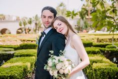 a bride and groom pose for a photo in front of a formal garden setting at their wedding