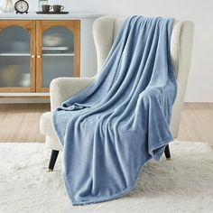 a chair with a blue blanket on it in front of a white rug and wooden cabinet